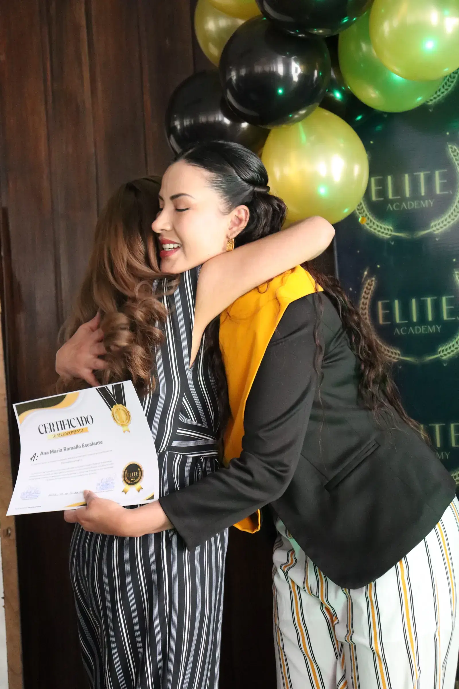 Abrazo entre una docente y una graduada con su certificado