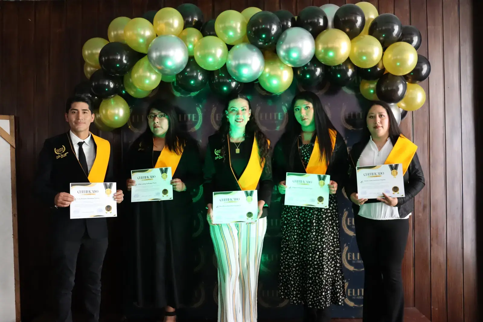 Egresados con sus certificados frente al arco de globos